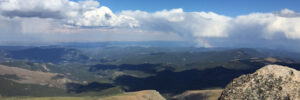 view from top of peak with mountains in foreground, some clouds and faint rainbow in the sky CKeller Law Firm Colorado